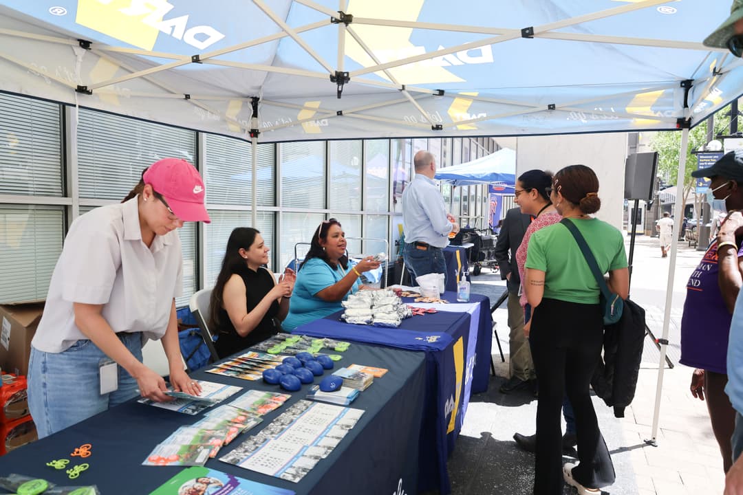 DART staff members hand out informational and promotional items to people under a DART-branded tent