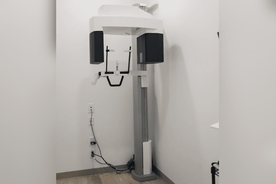 Panoramic dental X-ray machine mounted on a vertical column in a corner of a clinic room.