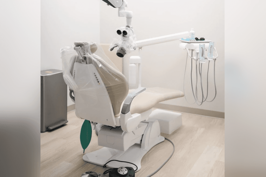Dental chair with overhead light and tools in a clean exam room with wood floor.