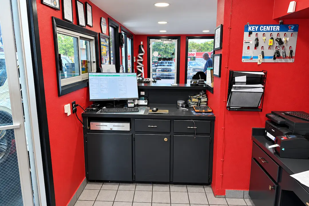 Auto shop front desk with red walls, computer, cash drawer, and Key Center display board on wall.