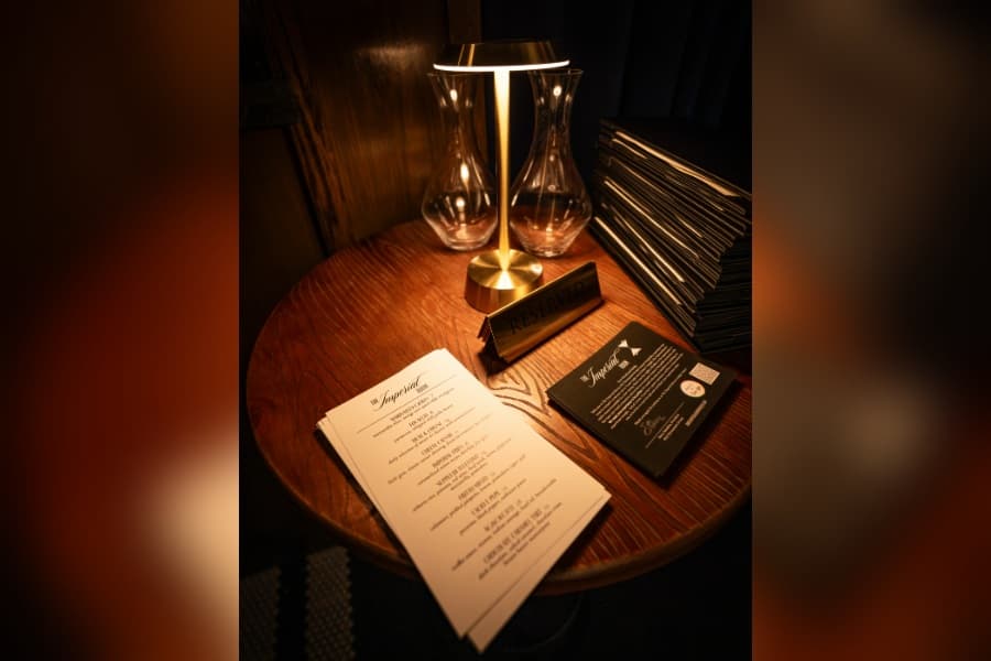 Dimly lit wooden table with menus, a brass lamp, glass decanter and a "Reserved" sign in a restaurant.