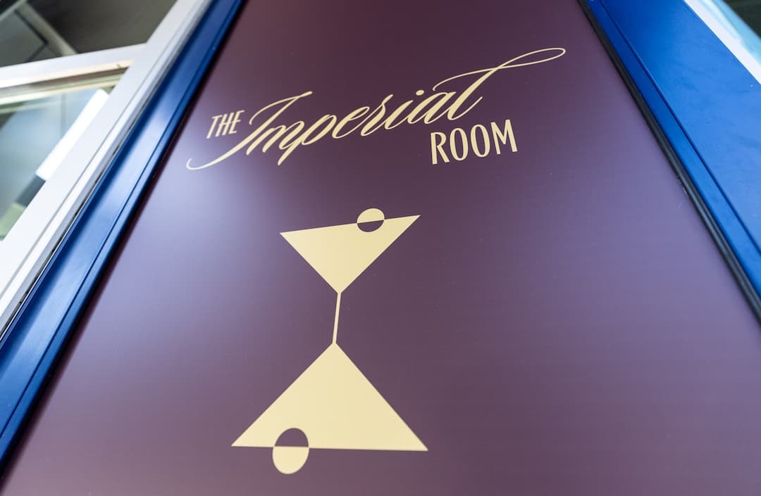 Purple sign reading "The Imperial Room" in gold with a stylized martini glass logo.