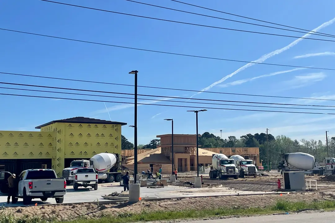 Construction site with cement mixer trucks, pickup trucks, and workers near partially built commercial buildings under a blue sky.