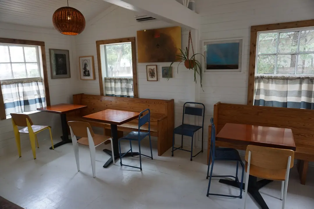 The interior of El Tigre, with moder, wooden benches and multicolored chairs. Artwork lines the walls, along with a plant.