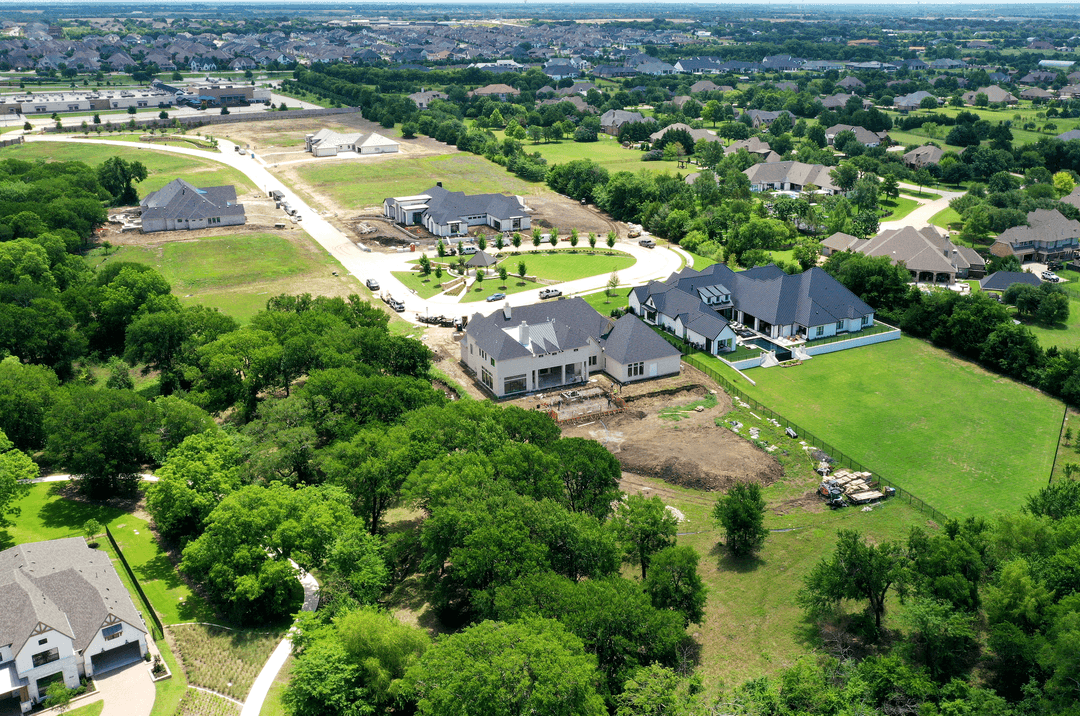 Aerial view of a new luxury home development with large houses under construction amid suburban sprawl and greenery.