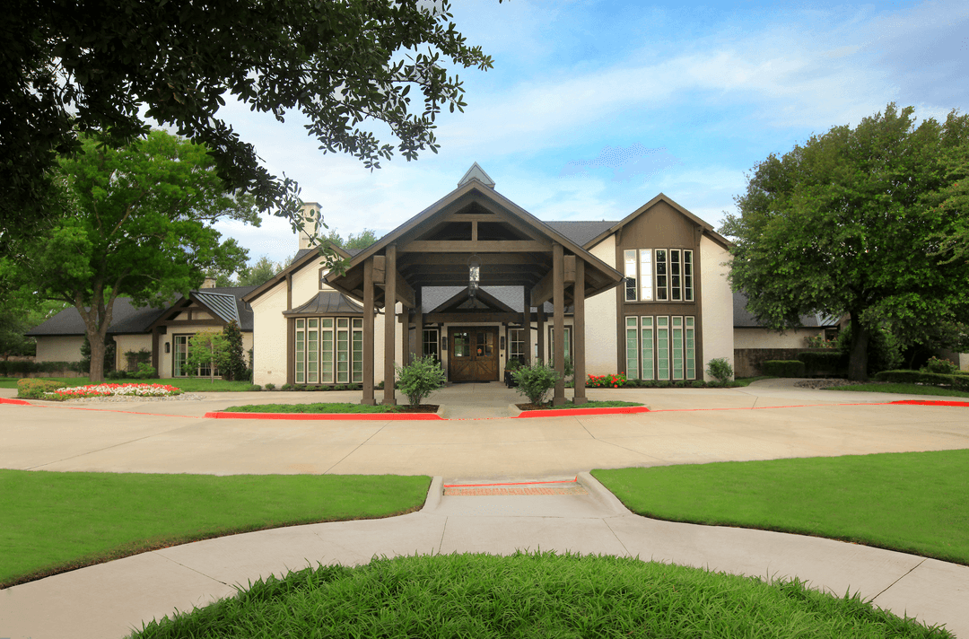Large upscale building with wood-beam entry, white brick exterior, landscaped lawns, and a wide concrete driveway.