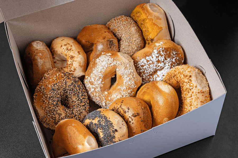 Assorted bagels including sesame, poppy seed, everything, and plain varieties in a white cardboard box.