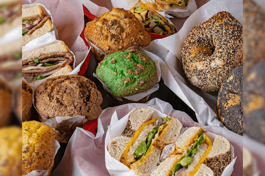 Assortment of muffins, bagel sandwiches, deli sandwiches, and wraps displayed in paper-lined baskets.