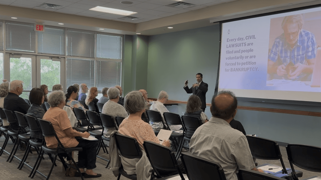 Man in suit presents a seminar on civil lawsuits and bankruptcy to a seated audience beside a projector screen.