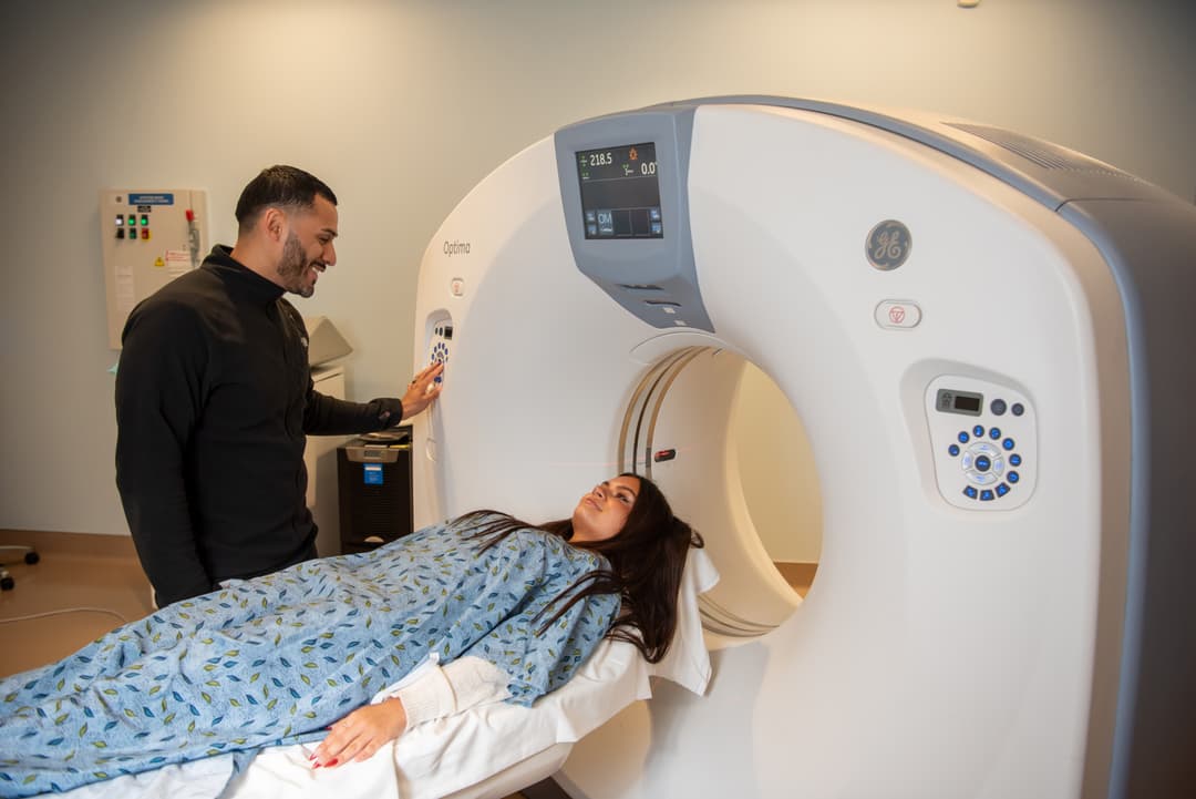 Technician smiles at a woman lying on the table of a GE CT scanner during an imaging exam.