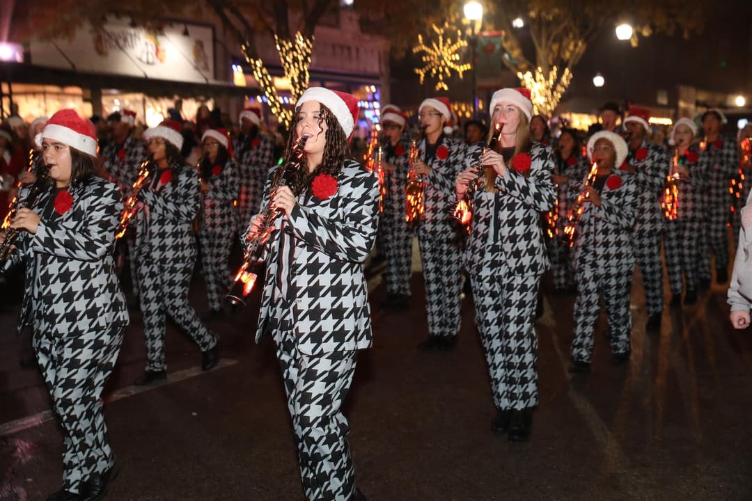Marching band in houndstooth suits and Santa hats plays clarinets in a nighttime Christmas parade.