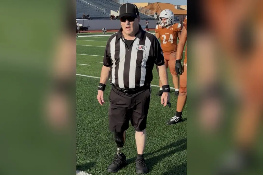 A football referee with a prosthetic leg stands on the field near a player in an orange uniform.
