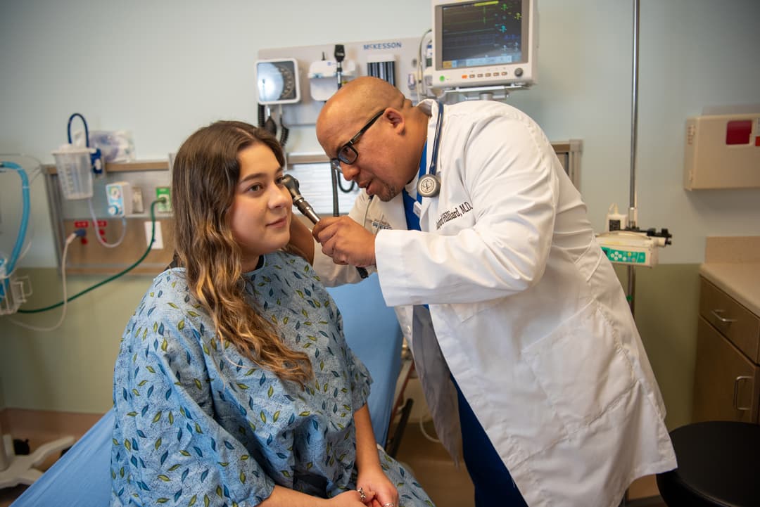 Doctor examines a patient's ear with an otoscope in a hospital exam room.