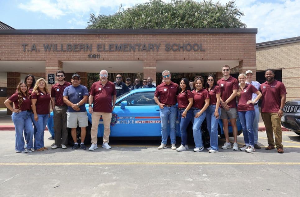 Group poses with Houston Police car outside T.A. Willbern Elementary School, many in maroon shirts.