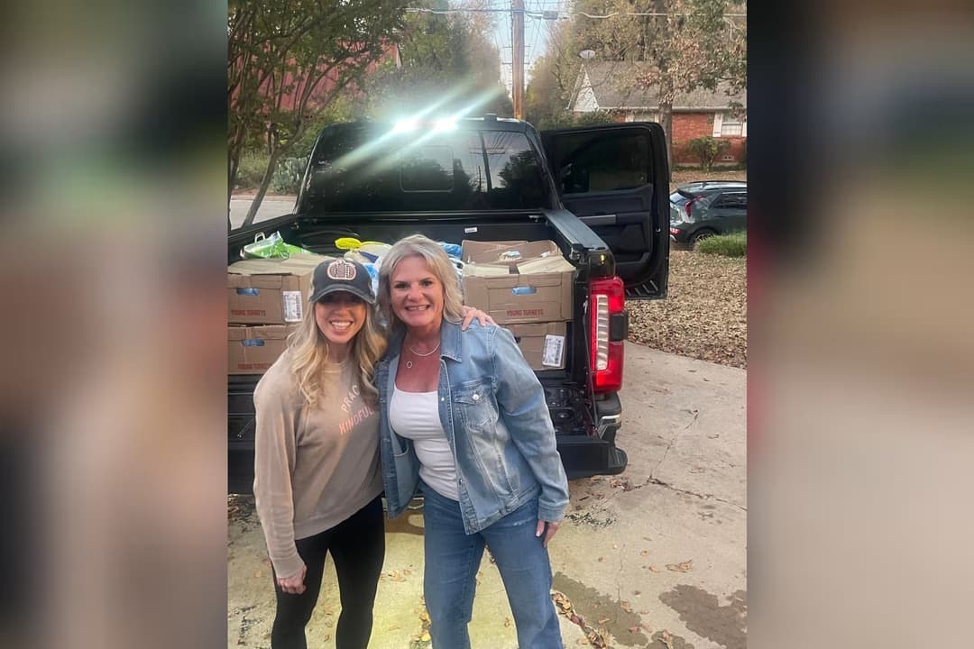 Two women smile in front of a black truck loaded with boxes of turkeys for donation.