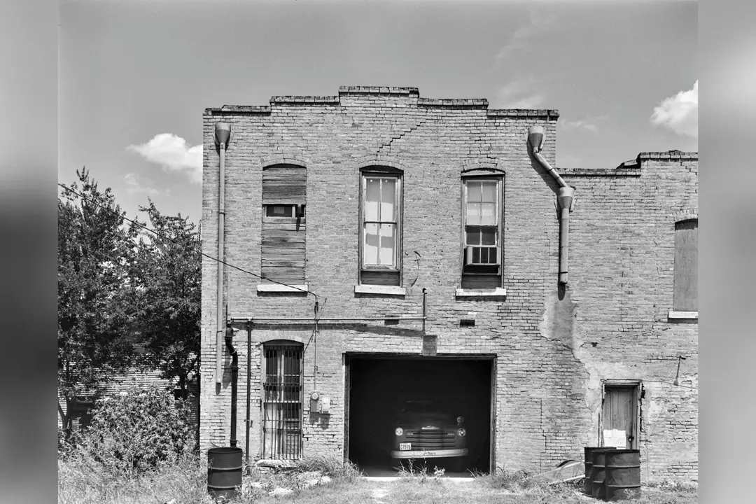 Weathered two-story brick building with a vintage truck parked in an open garage bay.