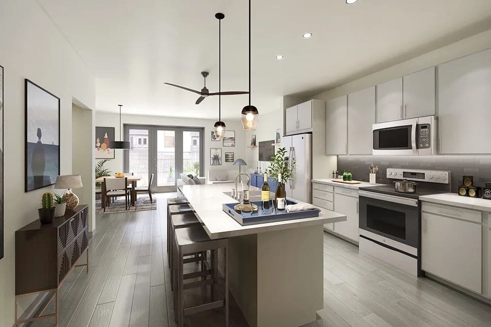 Modern open-plan kitchen with white cabinets, island with stools, pendant lights, and dining area near patio doors.