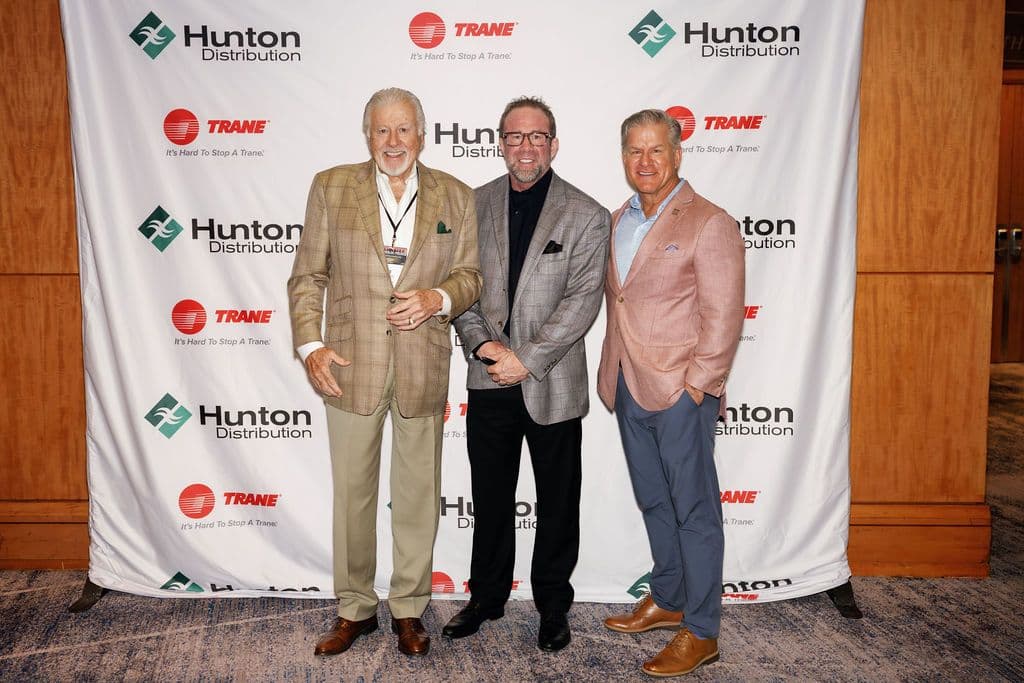 Three men in blazers pose smiling before a Hunton Distribution and Trane branded backdrop at an event.