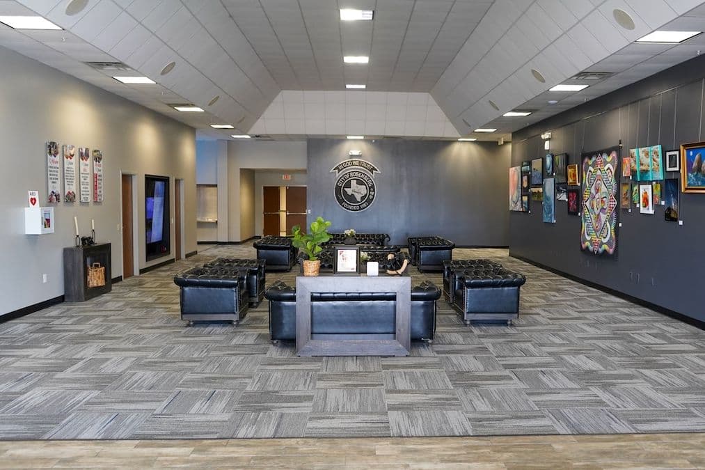 Spacious lobby with black leather seating, City of Rosenberg seal on wall, and colorful artwork displayed on gray wall.