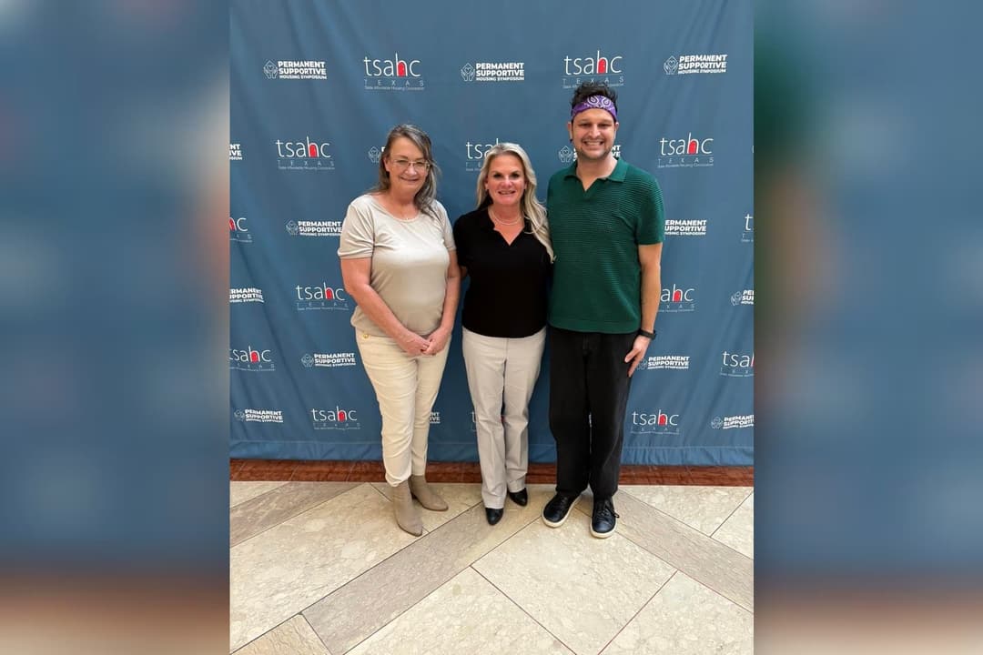Three people pose in front of a TSAHC Permanent Supportive Housing Symposium banner.