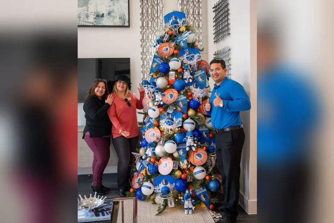 Three people posing beside a Christmas tree decorated with Dallas Mavericks basketball ornaments and pennants.