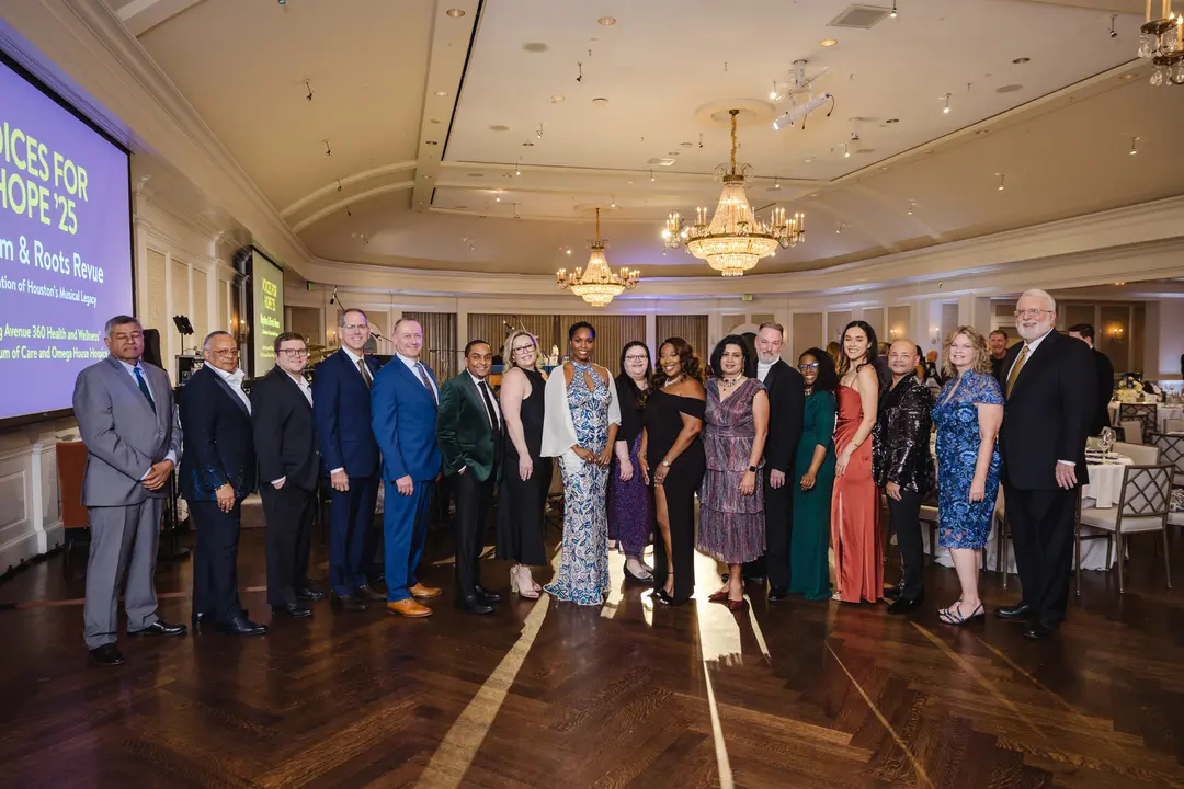 Group in formal attire poses in a ballroom with chandeliers at the Voices for Hope '25 gala event.