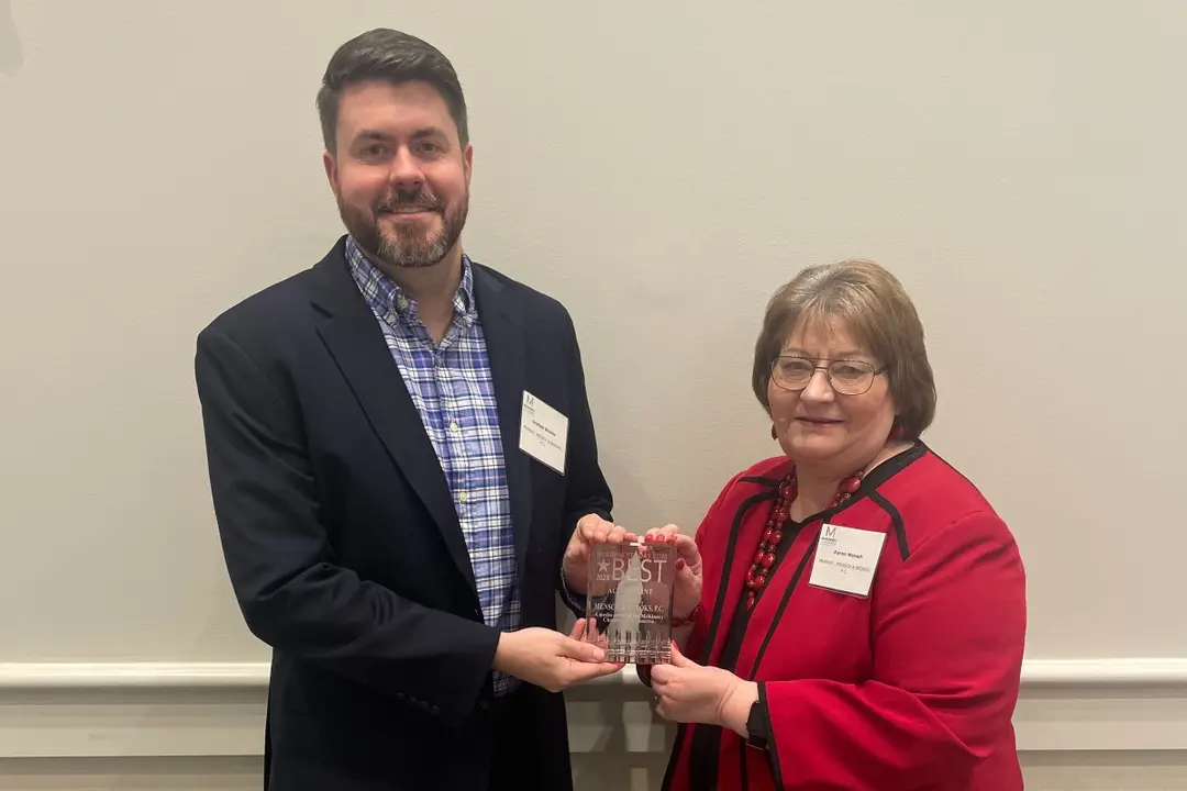 A man and woman with name tags hold a glass "Best" award plaque between them.