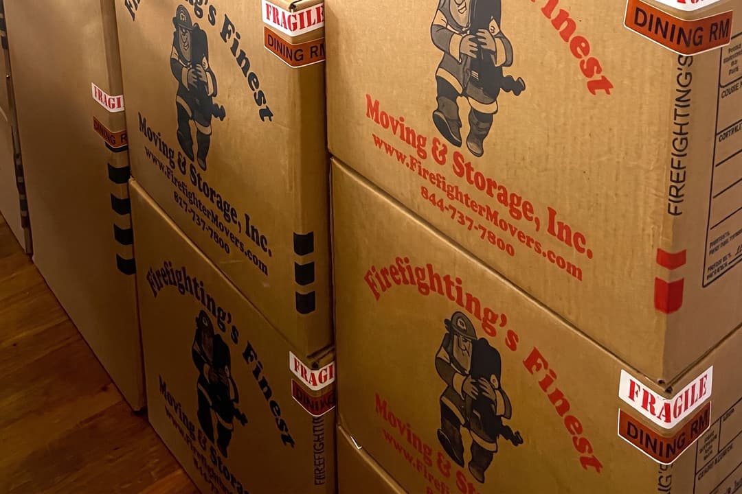 Stacked moving boxes labeled Firefighting's Finest Moving & Storage with Fragile and Dining Room stickers.