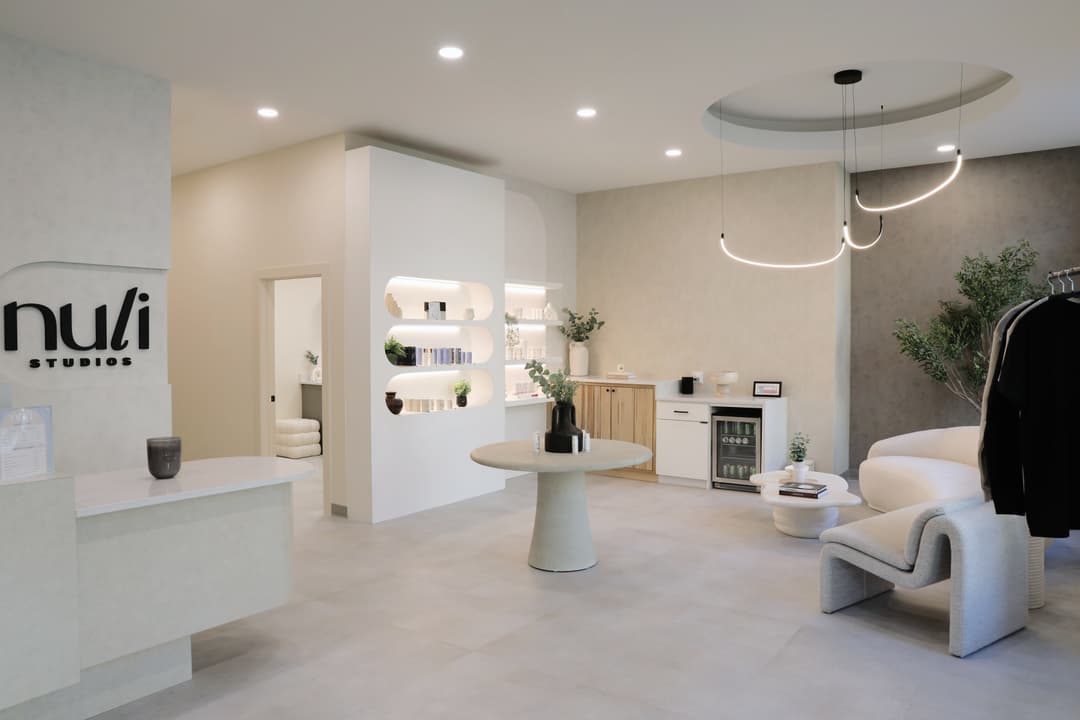 Modern Nuli Studios lobby with reception desk, logo wall, lit product shelves, boucle chairs and plants.