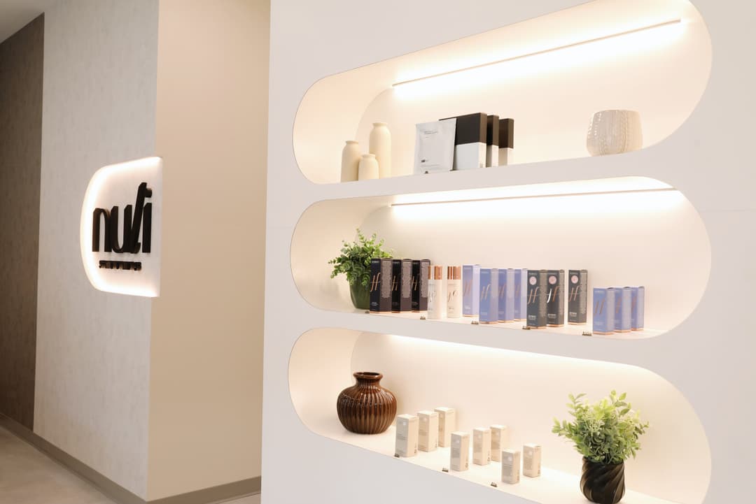 Illuminated arched wall shelves display skincare products, vases and plants beside a "nufi Studios" logo sign.