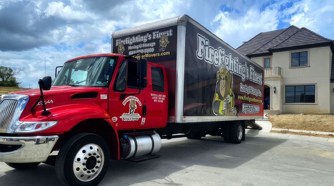 Red Firefighting's Finest Moving & Storage box truck parked in front of a large two-story home.