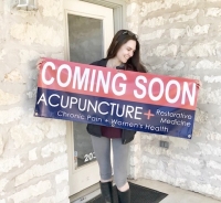 A photo of a woman holding a "coming soon" sign for Acupuncture + Restorative Medicine