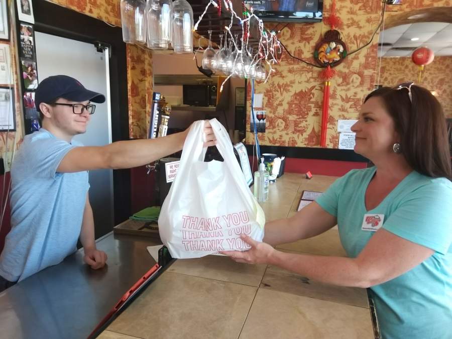 Shanghai Express Assistant Manager Devon Ponce hands a takeout order to Waiter With Wheels co-owner and part time delivery driver Stacey Westphal. (Courtesy Waiter With Wheels)