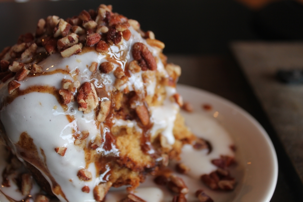 Stickee Cinnamon Roll ($3.23) is a signature dish that is baked fresh every morning and topped with cream cheese icing, caramel drizzle and pecans. (Sierra Rozen/Community Impact Newspaper)