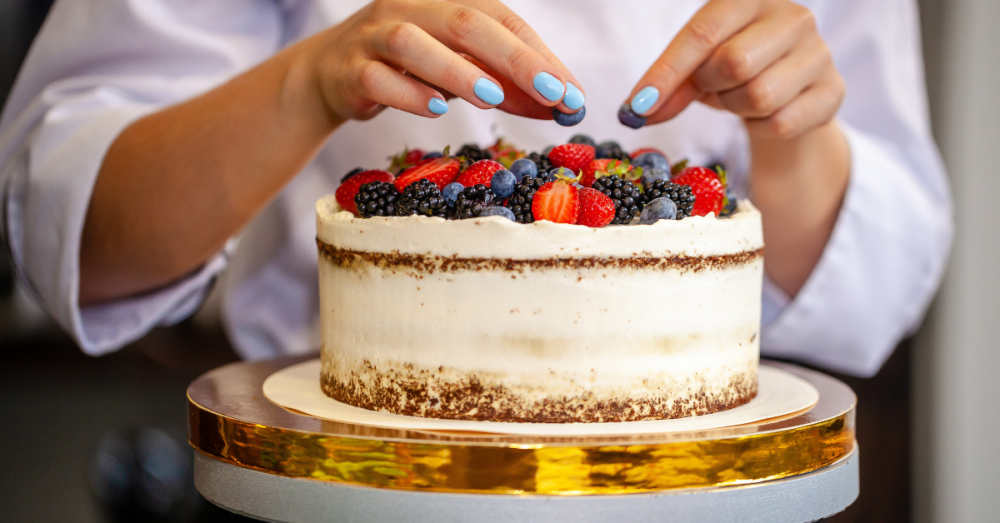 Hands decorate a cake with berries