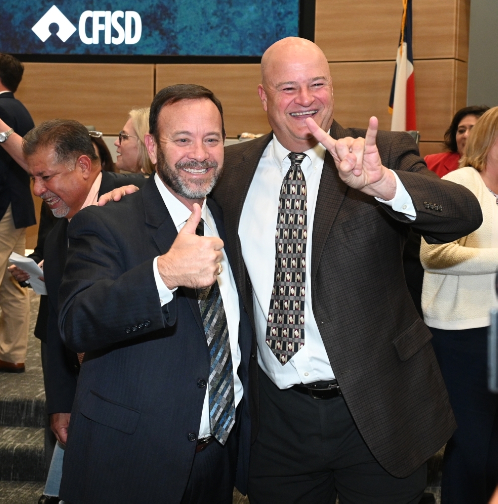 Cy-Fair ISD Superintendent, Doug Killian (left), and former superintendent Mark Henry support their alma maters at a Nov. 13 board meeting with Texas A&M University’s “Gig ‘em Aggies” and The University of Texas’ “Hook ‘em Horns” hand signals, respectively. (Courtesy Cy-Fair ISD)