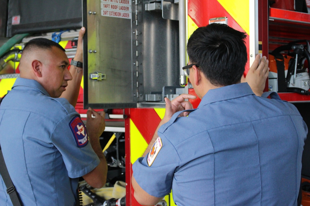 Firefighter Ricardo Roman (left) inspects the fire engine with colleague Steven Morales (right). (Kelly Schafler/Community Impact)
