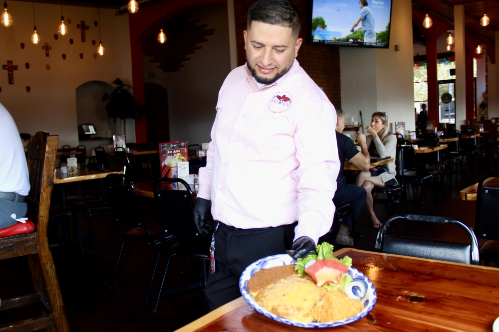 Owner Miguel Jaurigui serves a plate of enchiladas. (Jovanna Aguilar/Community Impact)