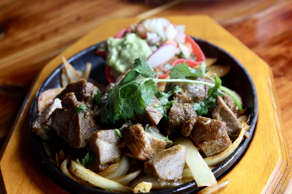 The carnitas plate ($16.99) incudes pork carnitas on a plate of grilled onions served with rice beans and pico de gallo, guacamole, tortillas and a secret taco sauce. (Jovanna Aguilar/Community Impact)