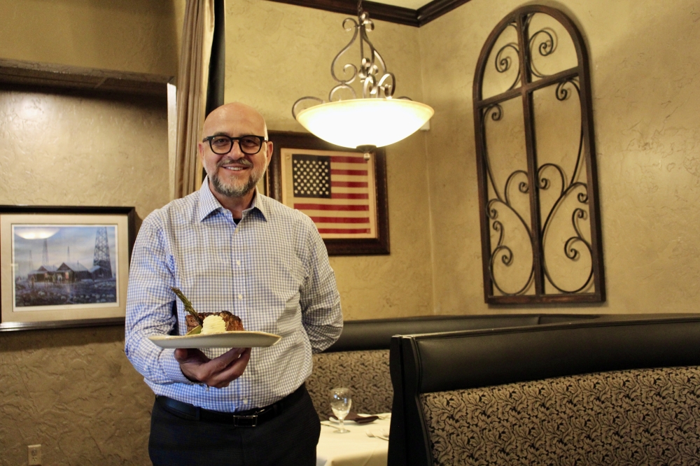 Sam Kurti holds a pork chop at his restaurant Dulcino's Italian Steakhouse. (Jovanna Aguilar/Community Impact)