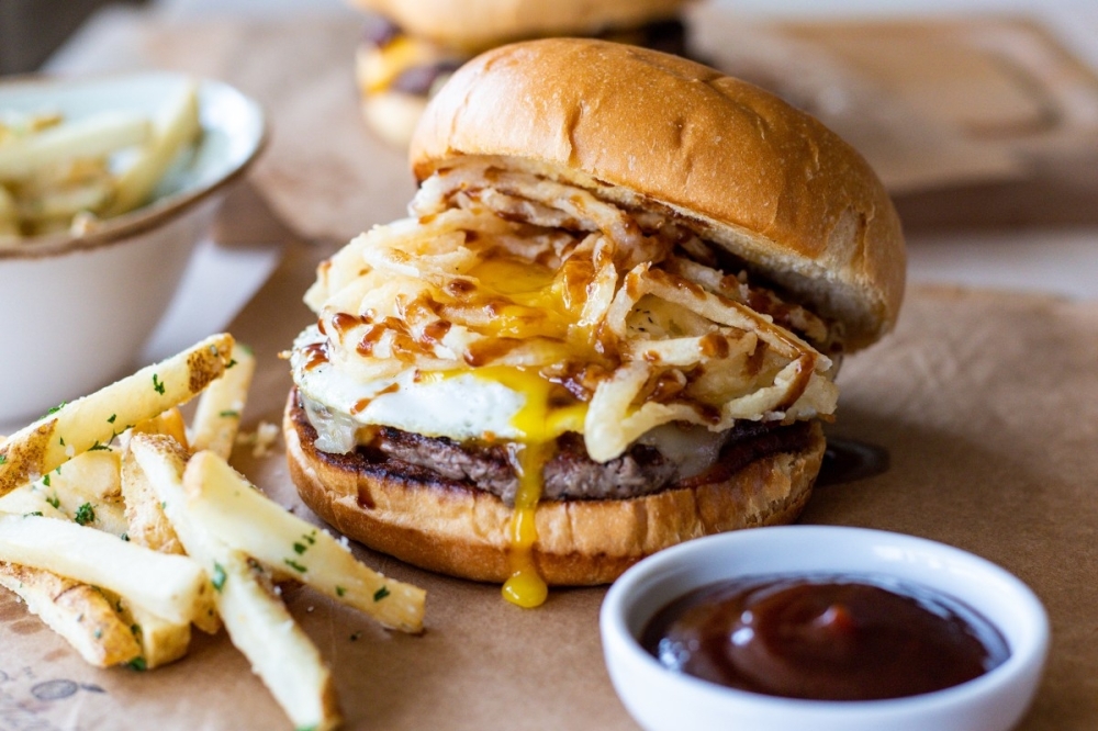 The JapaJam Burger ($15) is a 6-ounce all-beef patty with tomato jam, pepper jack cheese, tempura onion strings, a fried egg and Chinese barbecue sauce. (Courtesy The Peached Tortilla)