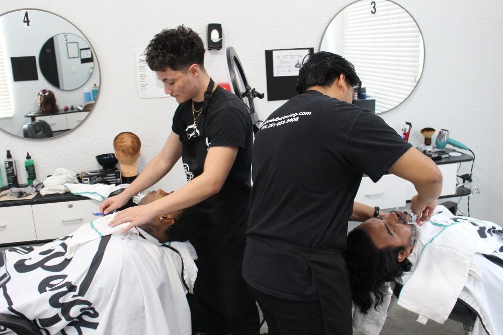 Jean Percy School of Barbering students David Martinez (left) and Daniel Cruz (right) practice shaving with a straight razor during a Jan. 14 class. (Ryan Reynolds/Community Impact)