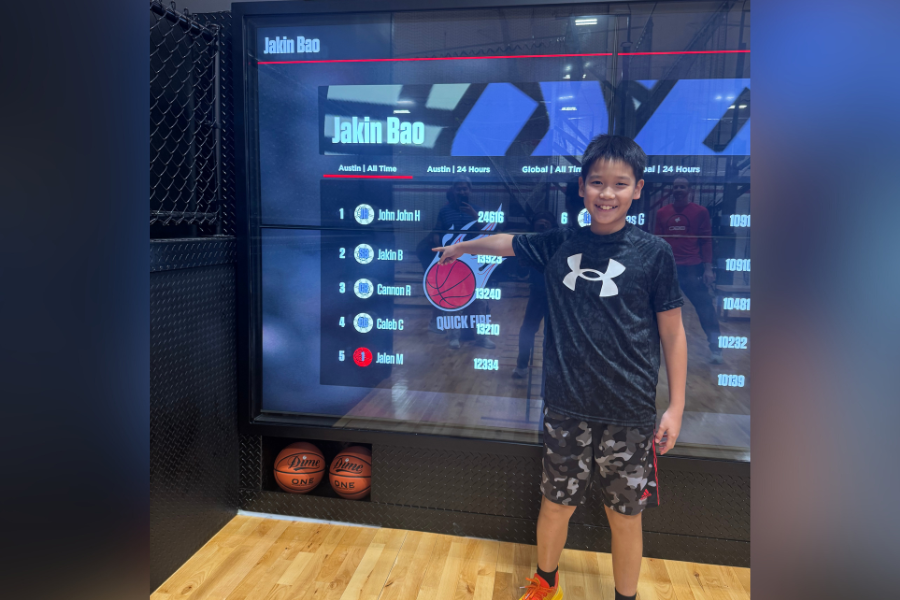 Youth basketball player at Shoot 360 Austin standing in front of interactive leaderboard display showcasing high scores and performance rankings.