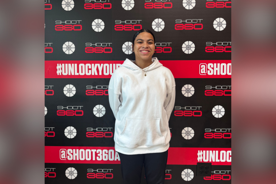 Female basketball player posing in front of branded Shoot 360 Austin backdrop featuring #UnlockYourGame and @Shoot360Austin, highlighting youth training, athlete development, sports technology, skill tracking, and performance training environment.