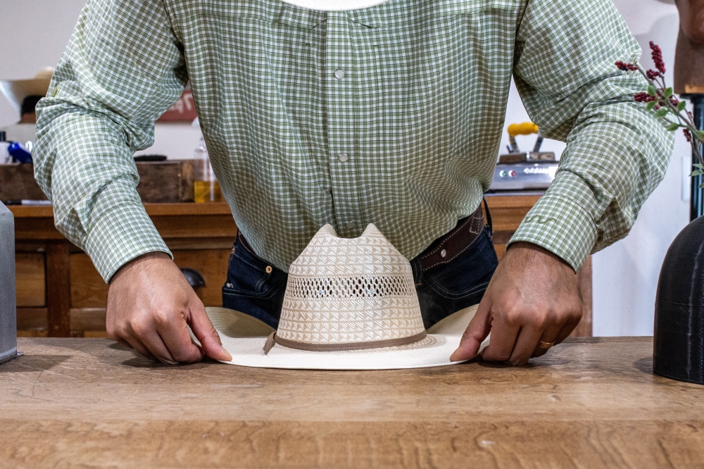 Emilio Rangel shapes the brim of one his house brand hats. (Joel Valley/Community Impact)