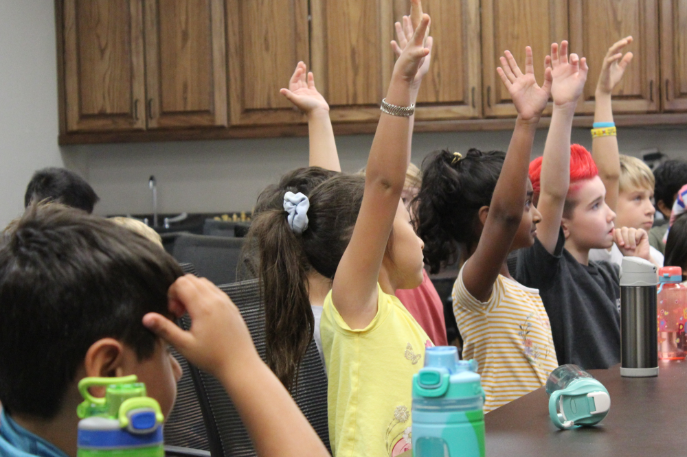 Students raising their hands in chess class Houston