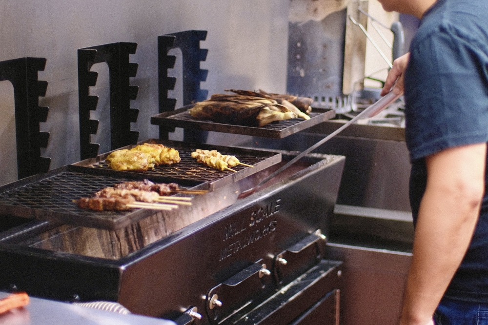 Grilled chicken and satay skewers cook over an open flame inside Sate Texas, where dishes are prepared to order at restaurant. (Manny Holguin / Community Impact)